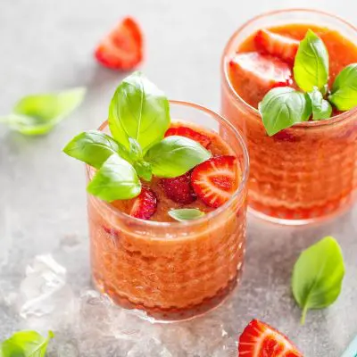 Top view of two Strawberry Basil Cocktails garnished with fresh basil, presented on a light grey surface