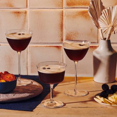 Front view of three decadent Espresso Martini cocktails served with sweet and savory snacks