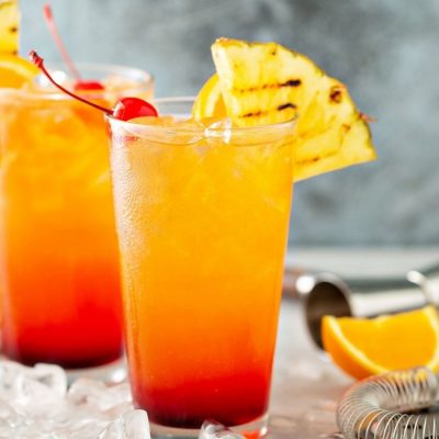 2 tall glasses of Italian Sunrise cocktails garnished with pineapple