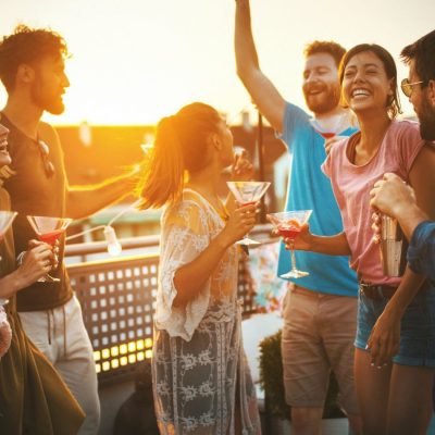 A group of diverse friends having a great time at an outdoor cocktail party hosted on a rooftop at dusk