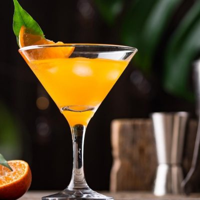 Orange-colored Bronx cocktail served in a martini glass with a wedge of fresh orange