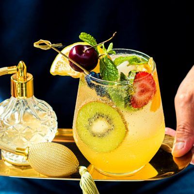 Close up front view of a fruity Kiwi and Mint Mocktail held on a golden-hued serving tray by a server in a black short-sleeve shirt