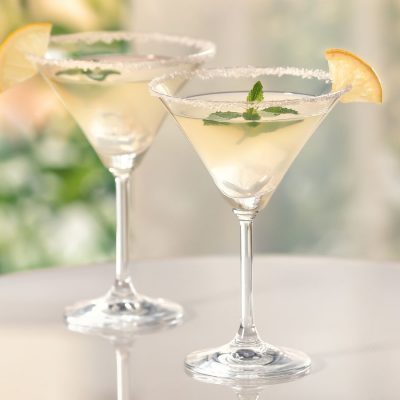 Two pretty Lemon Drop Martinis on a glass table, garnished with a sugar rim each