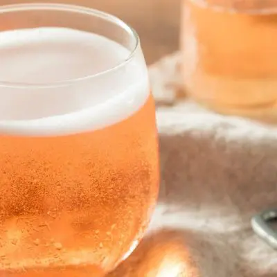 Sparkling apple cider cocktail on a beige cloth with a bottle opener