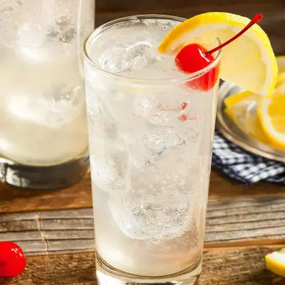 Two refreshing Tom Collins cocktails on a wooden surface, garnished with lemon slices and cherries