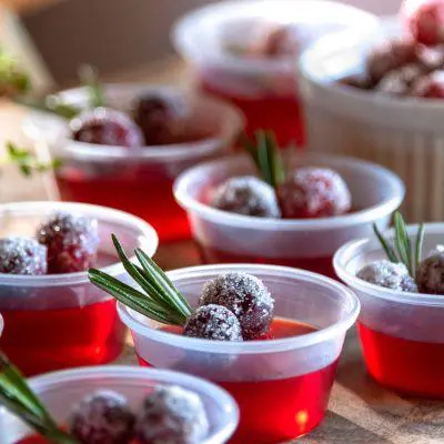 A tray of red Jello Shots garnished with berries and rosemary