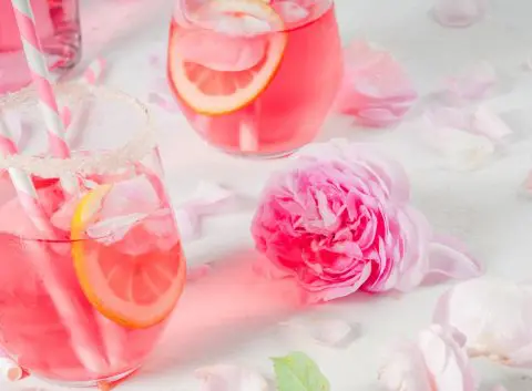 Three pretty pink Mother's Day cocktails against a white backdrop with a pink rose and some petals scattered for a touch of whimsy