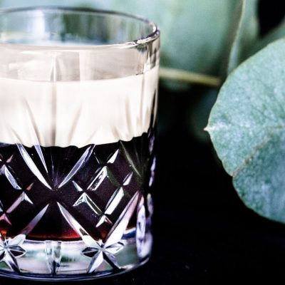 A creamy Baby Guinness Shot against a dark backdrop decorated with a sprig of pennygum