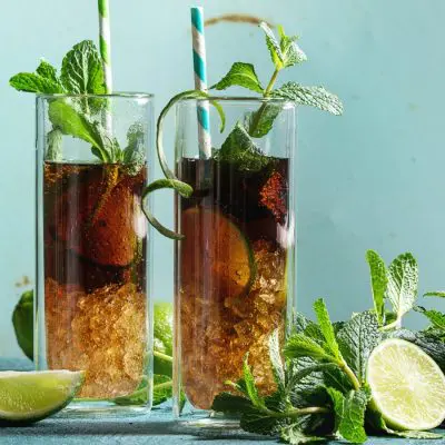 Two Cuba Libre cocktails served in a tall glasses with ice, lime and mint garnish