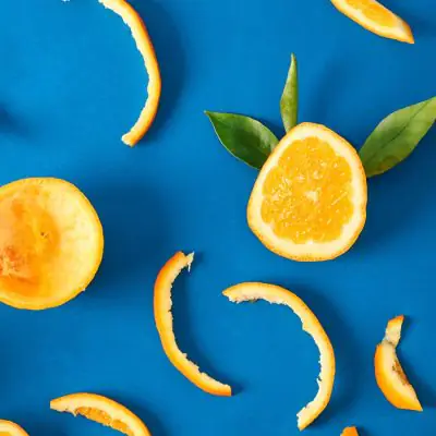 Close up top view of a collection of orange peels and slices on a bright blue backdrop