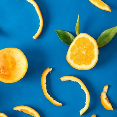 Close up top view of a collection of orange peels and slices on a bright blue backdrop