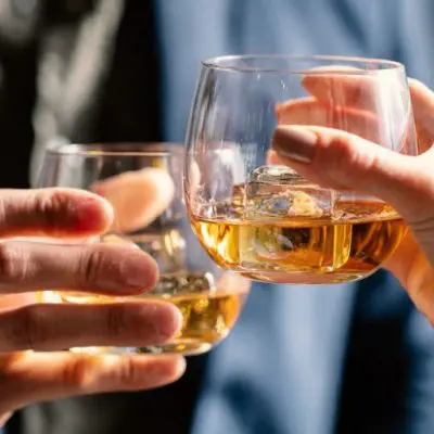 Close up of a couple clinking glasses of whiskey with clear ice cubes