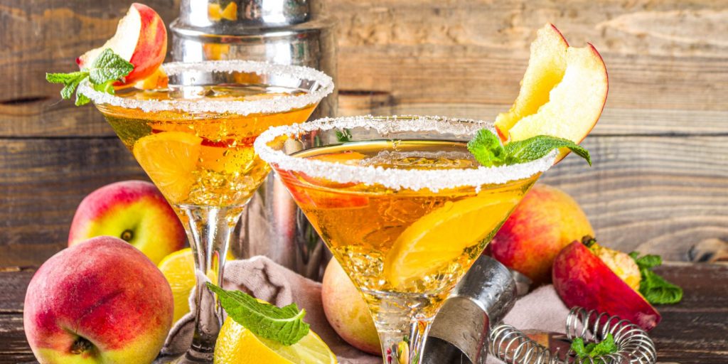 Close up of two sugar-rimmed Peach Martinis against a rustic wooden backdrop