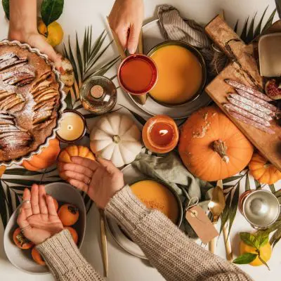 Top view of a very festiive Friendsgiving table dressed in wonderful fall colours with friends sharing food and passing bowls to one another