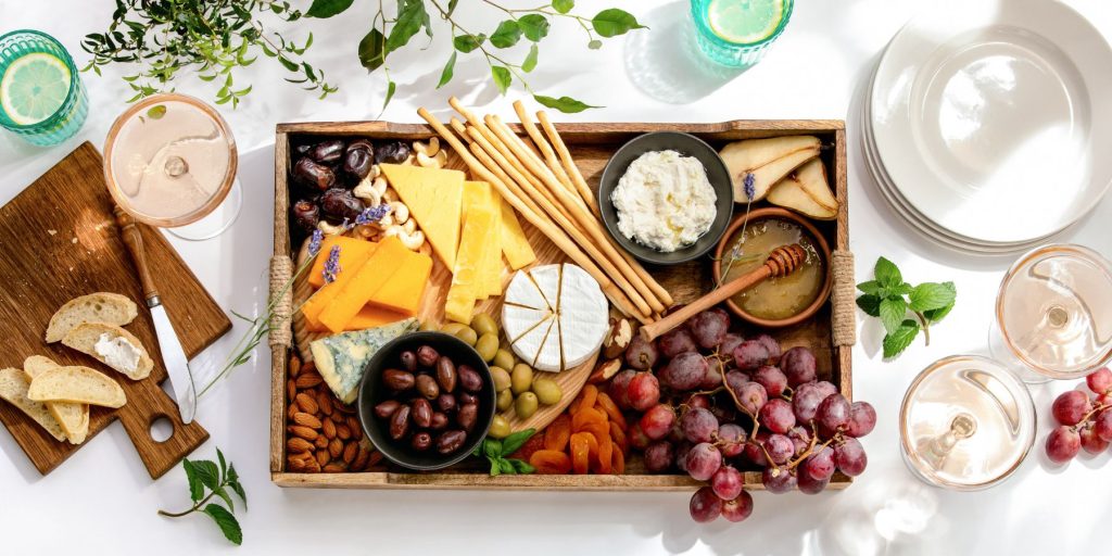 Top view of a charcuterie platter on a white table surrounded by pretty tableware and glasses of summery cocktails