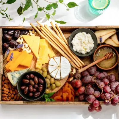 Top view of a charcuterie platter on a white table surrounded by pretty tableware and glasses of summery cocktails