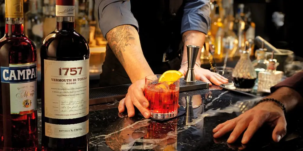 A bartender serving a Negroni cocktail to a customer at a bar