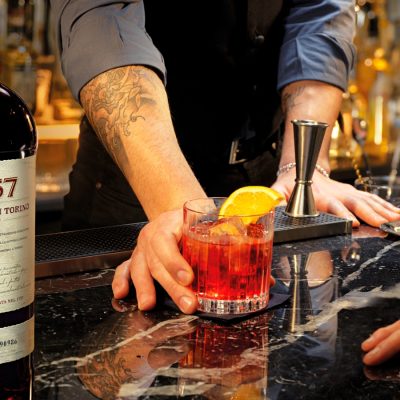 A bartender serving a Negroni cocktail to a customer at a bar