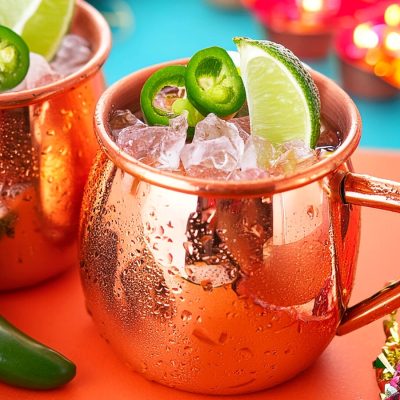 Two Spicy Mexican Mule cocktails served in copper mugs and garnished with sliced jalapeños and lime wedges