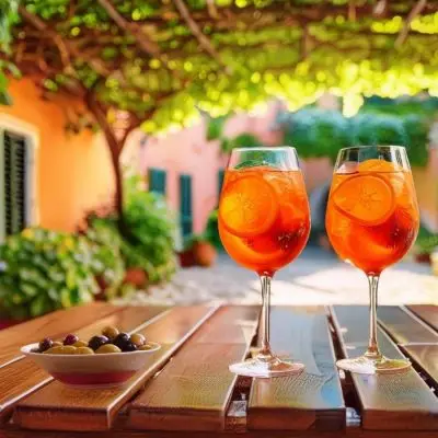 Two Aperol Gin cocktails on a wooden table outside in a courtyard beneath a vine trellis on a sunny day