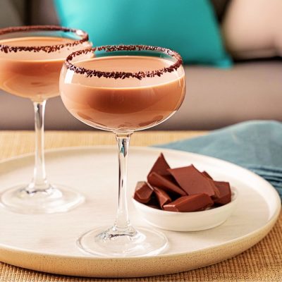 Two Mudslide cocktails with chocolate rims, served in coupe glasses on a coffee table in a lounge