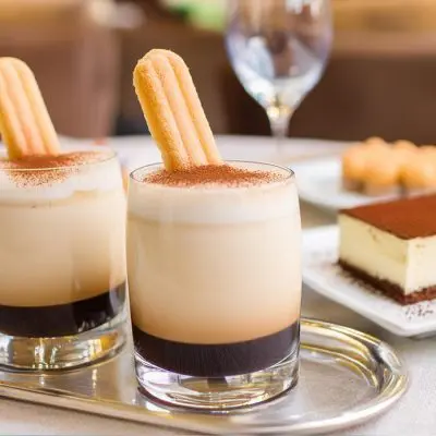 Close up of two Tiramisu White Russian variations served with lady finger biscuit garnish and a slice of tiramisu on the side