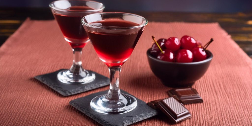 Two Mini Manhattan cocktials next to a bowl of cherries and pieces of dark chocolate
