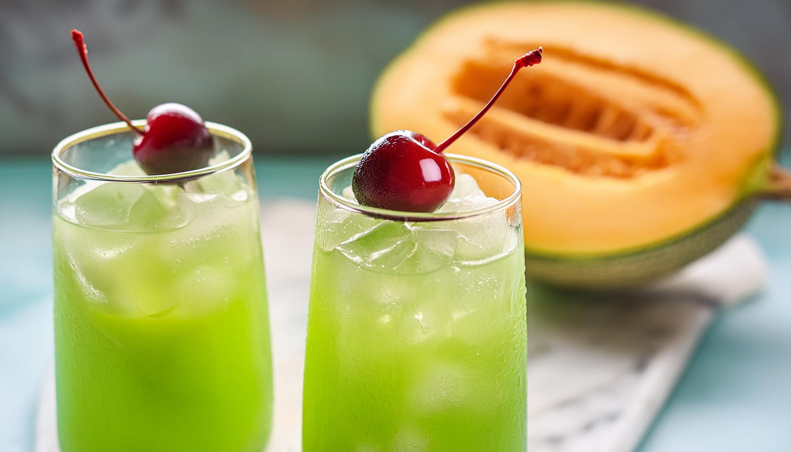 Two bright green Tokyo Tea cocktails with Luxardo cherry garnish