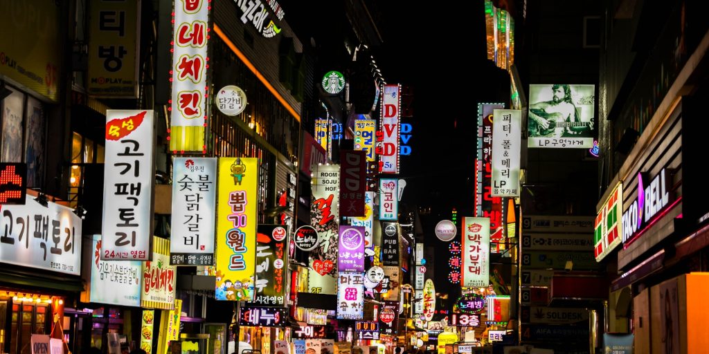 Wide view of a Korean bar avenue with lots of neon signs in Korean later at night, already dark