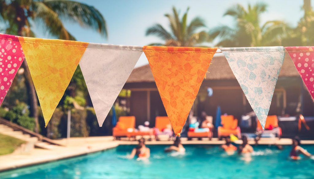 Closeup of colourful bunting hanging over a pool, people swimming in the background