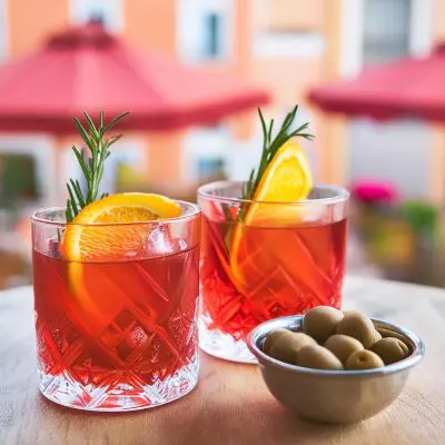 How to choose the best vermouth for a Negroni - two Negroni cocktails garnished with orange slices and rosemary on a table outside next to a bowl of olives