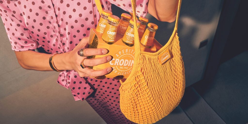 A close-up of a woman's hands holding a pack of Crodino Non-Alcoholic Spritz aperitif bottles