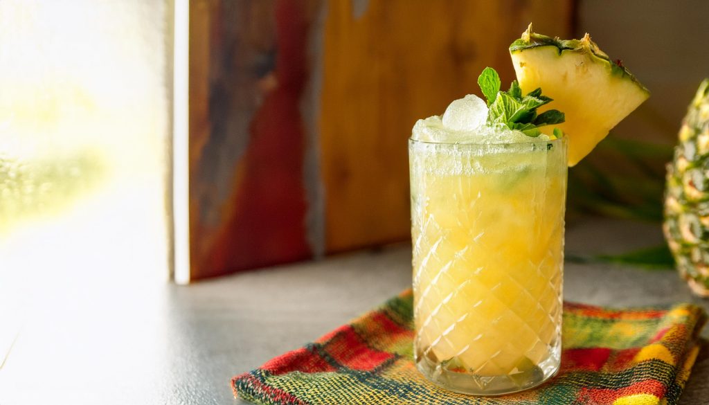 A pineapple tequila cocktail in a highball glass with pineapple and fresh mint garnish 