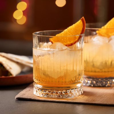 Two Montelobos Mezcal Old Fashioned cocktails with orange wedge garnish served with a burrito