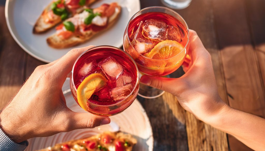 Overhead shot of two hands clinking together two Campari Spritz cocktails