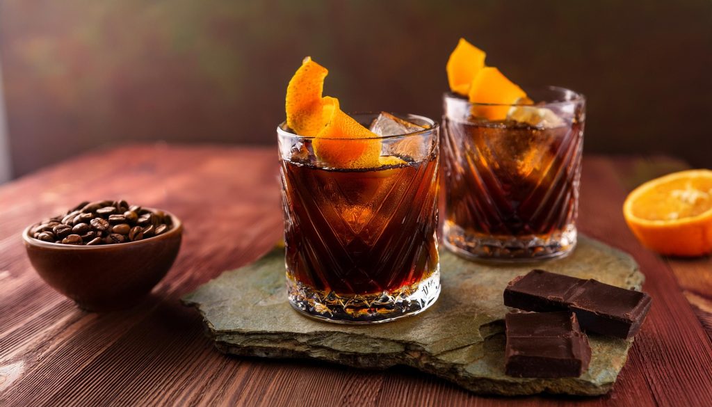 Two Coffee Negroni cocktails with orange twist garnish, served on slate with dark chocolate