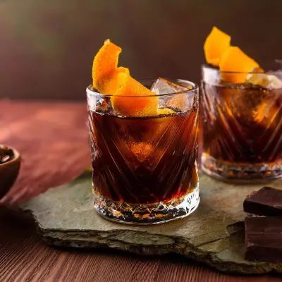 Two Coffee Negroni cocktails with orange twist garnish, served on slate with dark chocolate