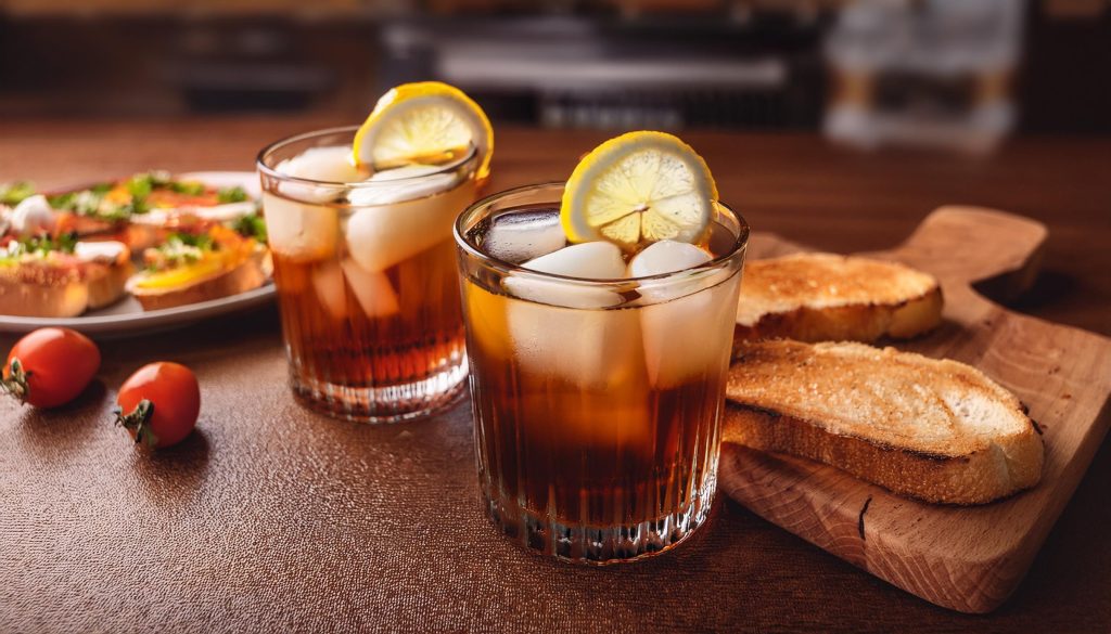 Two Cynar Negroni cocktails with lemon wheel garnish, served with bruschetta