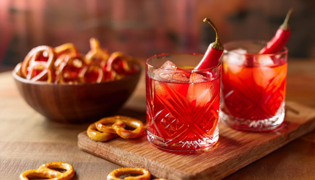 Two Spicy Negronis served on a wooden board with a bowl of pretzels