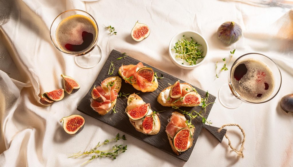 Overhead shot of crostinis topped with smoked salmon, figs and micro herbs served on a white linen table