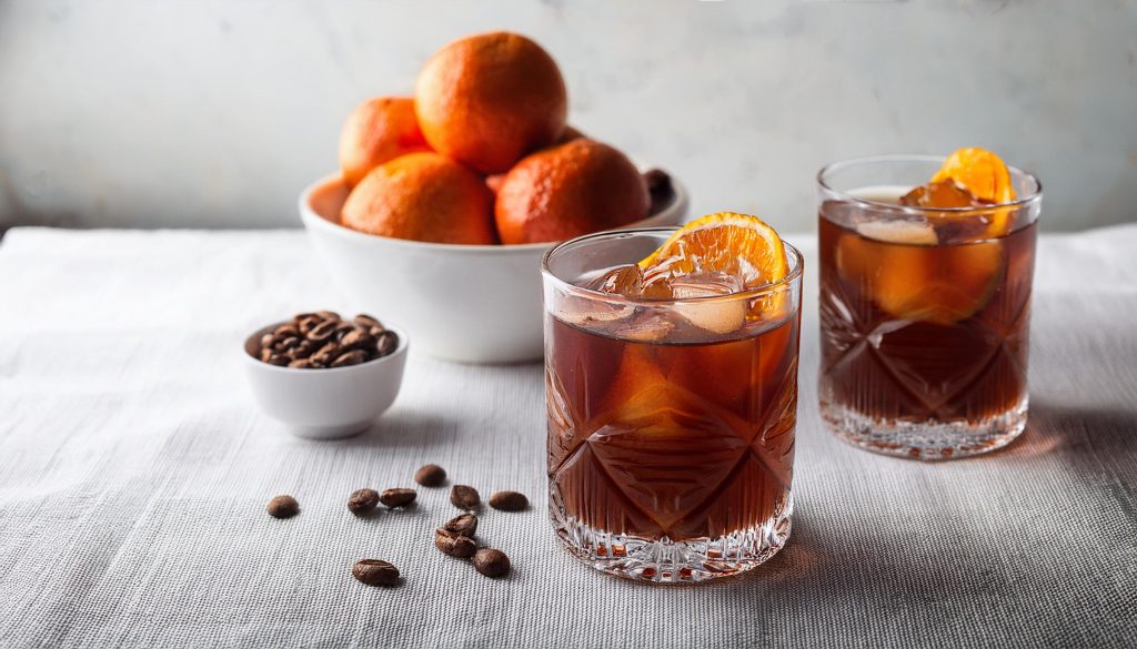 Two Coffee Negroni cocktails with orange wheel garnish, served on a white surface with a bowl of coffee beans and oranges 