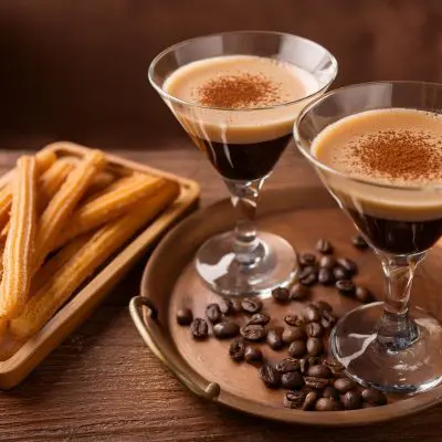 Two Tequila Espresso Martini Cocktails on a copper serving platter alongside a plate of churros in an inviting home setting