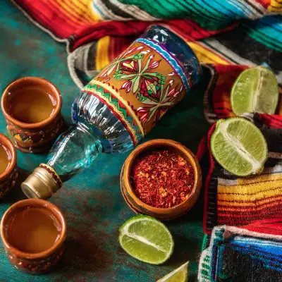 Top view of a selection of gifts for tequila lovers on a colorful fabric backdrop, including a bottle of tequila, interesting salts and more