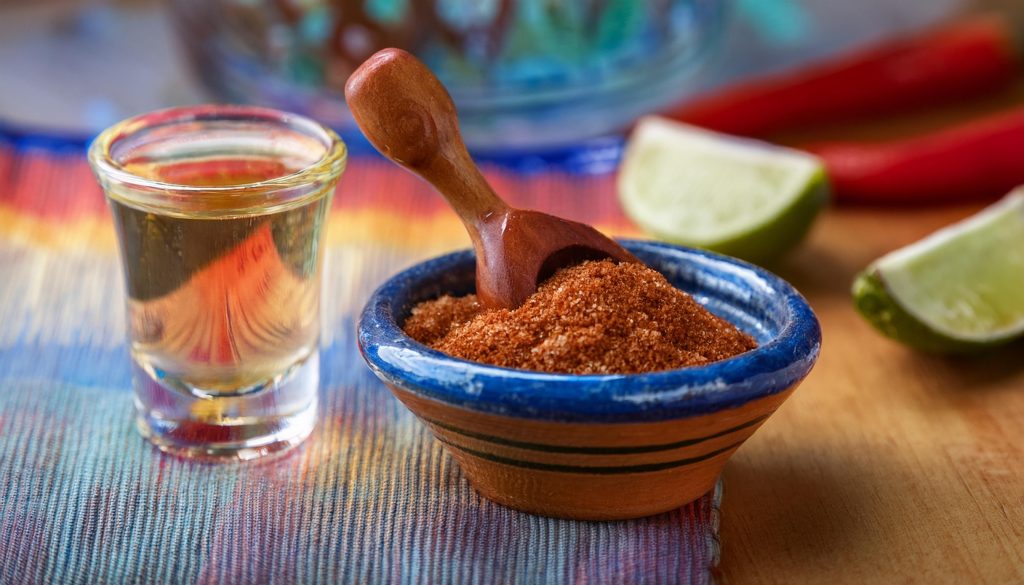 Close up of a bowl of chili and lime salt next to a shot glass of tequila on a counter in a home kitchen 