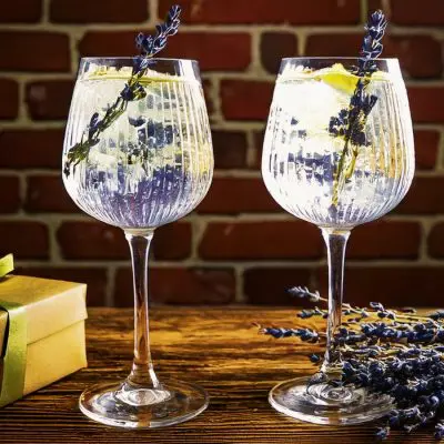 Close up of two gin and tonic cocktails garnished with lavender next to a gift for gin lovers on a wooden table in a welcoming home environment