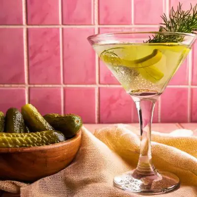 A Pickle Martini with fresh dill garnish, pink tiled background