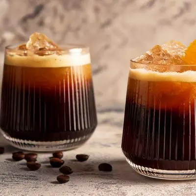 Two Carajillo Coffee cocktails with fresh orange garnish