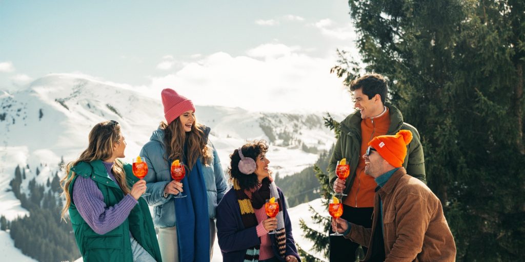 Friends enjoying Aperol Spritz cocktails, snowy mountains in the background