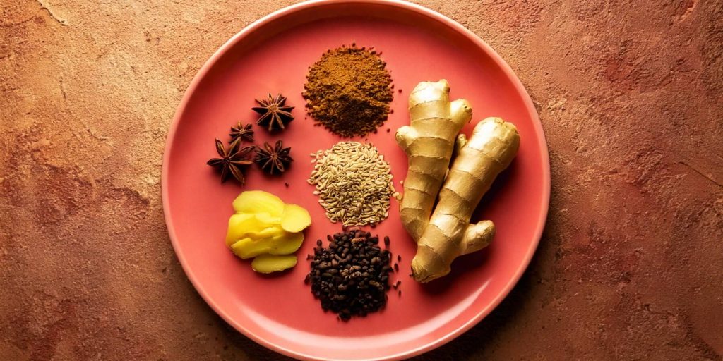 A colourful plate showcasing a variety of Asian spices, including star anise, cinnamon, fennel seeds, ginger, cloves, and ground spices, on a textured background.