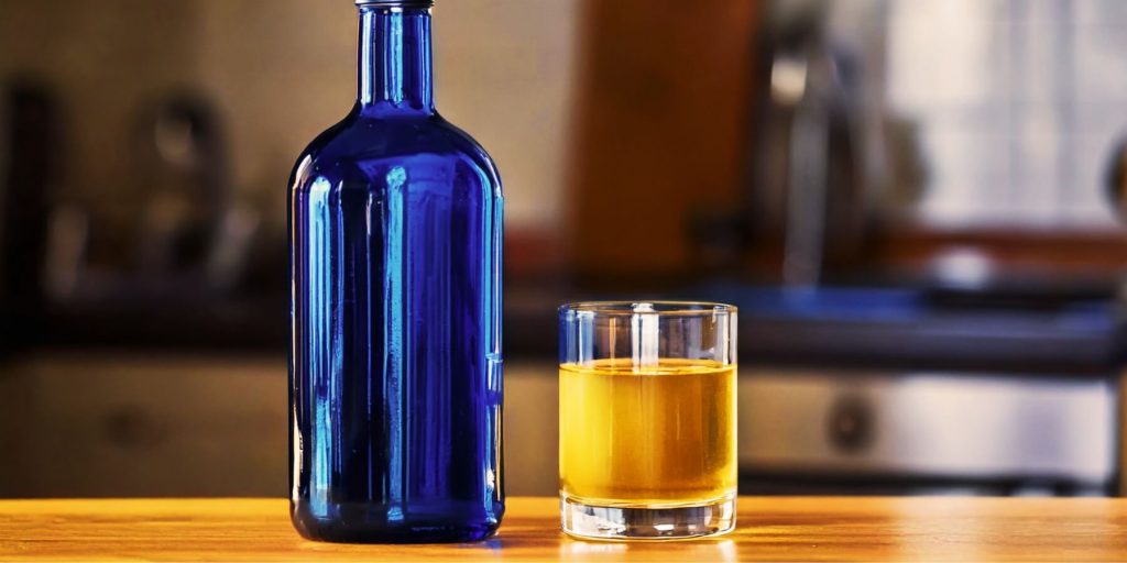 A minimalist setup of a blue bottle and a glass filled with sotol on a wooden surface, suggesting a sophisticated approach to enjoying the spirit.